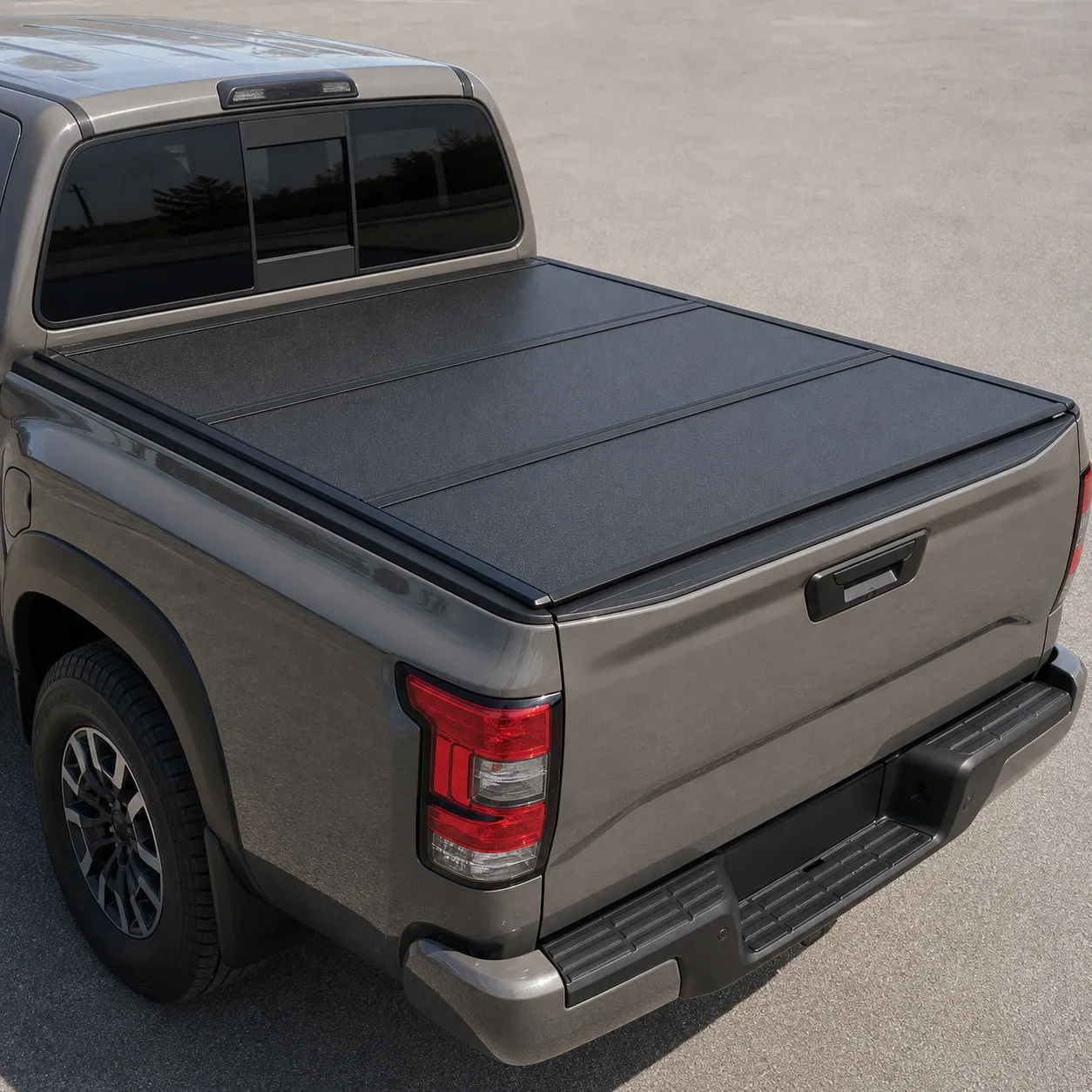 Black hard tri-fold tonneau cover closed over a Nissan Frontier bed showing the panel seams