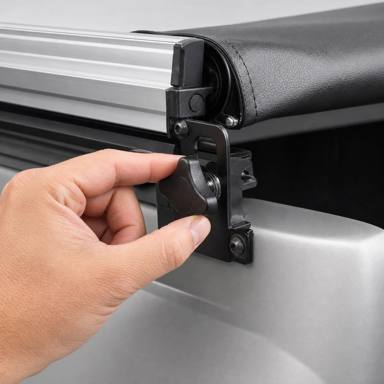 [Close-up of a hand turning a manual tension adjustment knob at the corner of a soft roll-up tonneau cover frame]