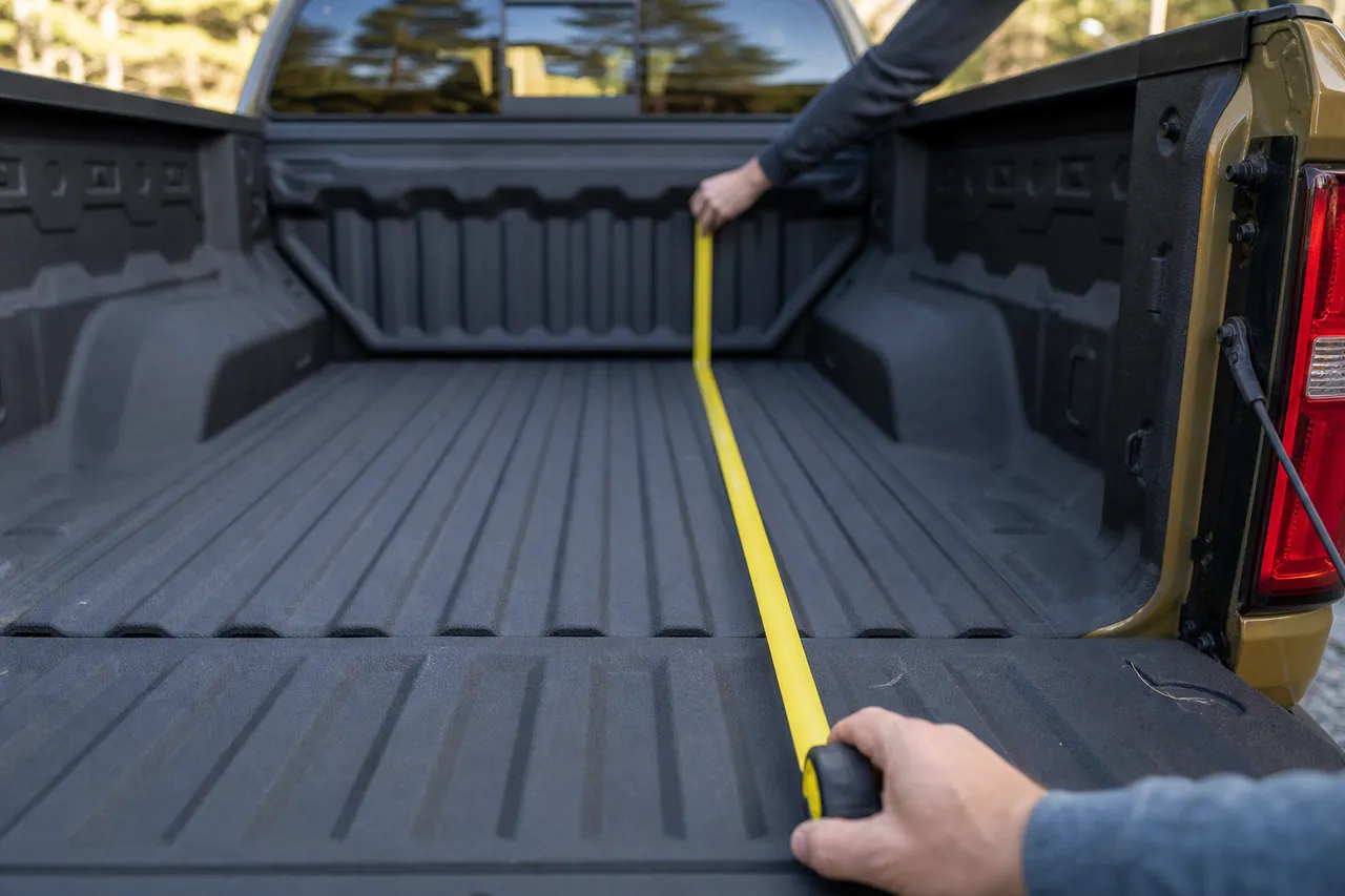 Tape measure laid across the inside of a Chevy Colorado bed rail showing the rail-to-tailgate measurement